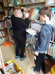 Dwaj chłopcy przy regale z książkami. Jeden z nich trzyma książkę w ręku.