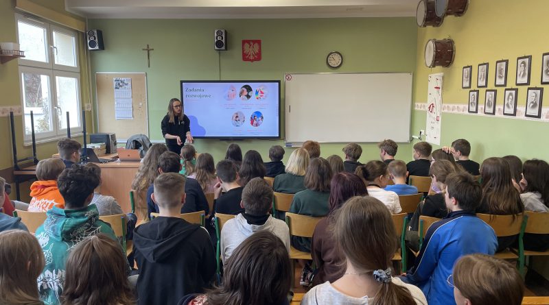 W klasie szkolnej uczniowie obserwują gościnię Panią Aleksandrę Raczyńską, studentkę psychologii, która przedstawia im prezentację dotyczącą rozwoju tożsamości człowieka.