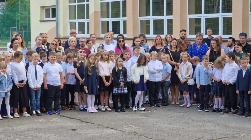 Uczniowie stoją obok siebie, a za nimi ich rodzice.