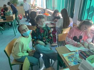 Uczniowie podczas przerwy na szkolnym korytarzu prezentują nosidła na książki i przybory szkolne w ramach akcji "Dzień bez plecaka"