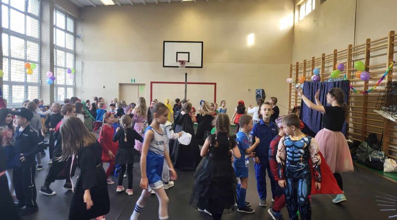 Dzieci tańczą w sali gimnastycznej. Animatorka pokazuje jak mają tańczyć.