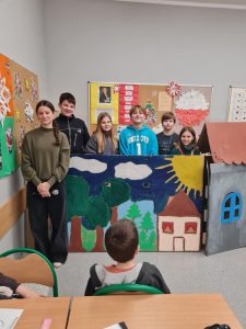 Uczniowie kl. VI d stoją za scenografią. Przed scenografią siedzi uczeń z klasy I b.