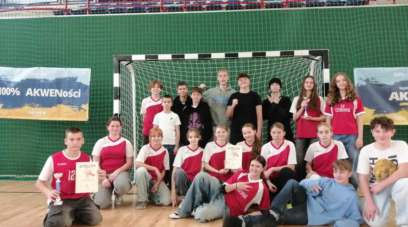 Zdjęcie 1: Na zdjęciu widzimy przedstawicieli drużyny SP Czerwonak ubranych w czerwone stroje sportowe ustawionych w szeregu przed bramką, pozujących z dyplomami oraz pucharem.