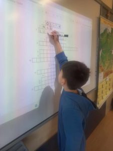 Chłopiec przy tablicy multimedialnej rozwiązuje krzyżówkę.