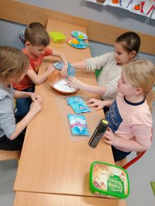 Trójka chłopców i jedna dziewczynka stoją wokół stolik. Ręce mają wysmarowane sztucznym śniegiem.