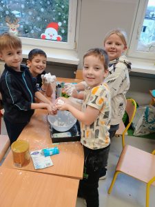 Przy stoliku stoją chłopcy i na czarnej blaszce łączą produkty, z których powstanie sztuczny śnieg.