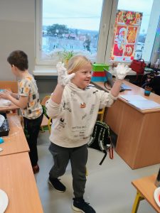 Uśmiechnięta dziewczynka podnosi do góry ręcę namoczone w białym puchu.