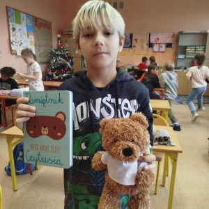 Chłopiec z poważną miną trzyma w jednej ręce maskotkę a w drugiej zeszyt z napisem Pamiętnik Czytusia