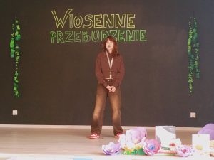 Na scenie stoi  dziewczynka ubrana w brązowe spodnie i bluzę.