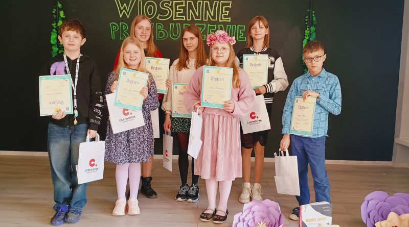 Na scenie stoją dzieci, które wygrały szkolny  konkurs recytatorski. W dłoniach trzymają dyplomy oraz drobne upominki.