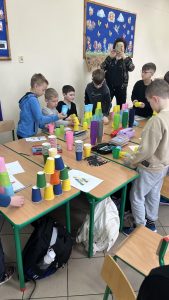 Uczniowie w sali lekcyjnej przy stolikach. Na stolikach wieże z kolorowych kubków – nauka programowania. 