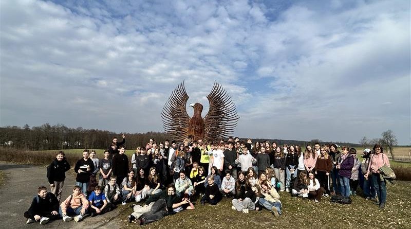 Bardzo liczna grupa młodzieży w szerokim planie na tle dużej figury orła.