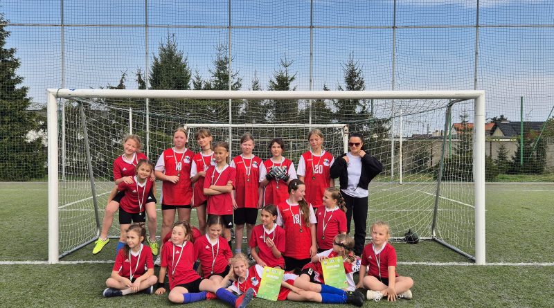 Zdjęcie grupowe dziewczyn z klas 3, 4, 5 po zakończonych rozgrywkach. Dziewczyny w czerwonych strojach sportowych