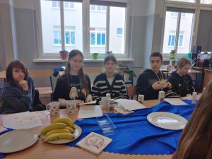 Na pierwszym planie znajduje się pięcioro uczniów: dwie dziewczynki, troje chłopców. Każdy z nich ma identyfikator i kubek, otrzymany z okazji Dnia Przyrodnika