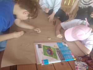 Uczniowie na szarym papierze grupowo wykonują totem z okazji Dnia Ziemi. Szkicują ołówkiem napis, hasło