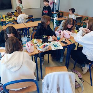 Uczniowie pracując w grupach wykonują pudełka na skarby przyrody. Na stolikach leżą farby, pisaki, kartki.