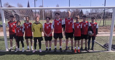 Na zdjęciu widzimy przedstawicieli drużyny SP Czerwonak ubranych w czerwone koszulki sportowe oraz czarne spodenki, ustawionych w szeregu przed bramką pozujących z piłką. Jako czwarty z lewej stoi bramkarz w żółtej bluzie.