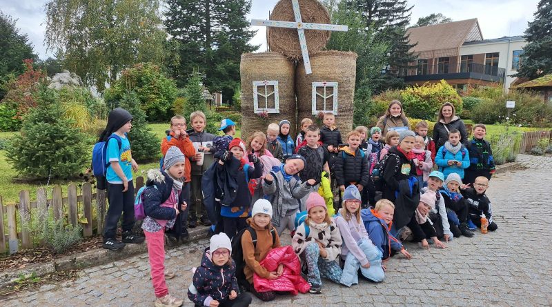 Zdjęcie grupowe klasy 1b i 1c z wychowawczyniami, a w tle wiatrak zbudowany ze słomy.