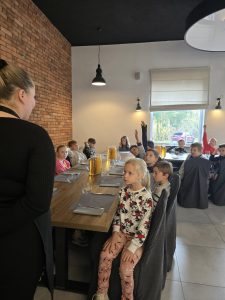 klasa przy stołach odpowiada na pytania pani kelnerki