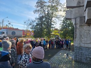 Uczniowie klas pierwszych stojący przed pomnikiem.