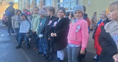 Uczniowie klasy pierwszej ustawieni na boisku, oczekują na uroczyste odśpiewanie Hymnu państwowego. 