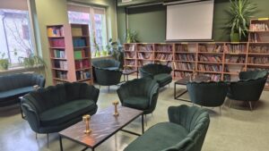 Widok na bibliotekę – na pierwszym planie fotele z stolikami, na drugim – regały z książkami.