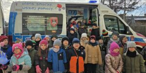 Uczniowie pozują do pamiątkowego zdjęcia na tle smoczego ambulansu.