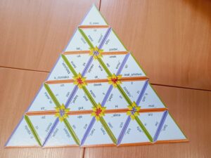 Na ławce leżą trójkątne puzzle – trimino, edukacyjna gra ortograficzna. Trójkąciki łączą się ze sobą, tworząc piramidę, a na każdym z nich znajduje się zadanie z trudnością ortograficzną.