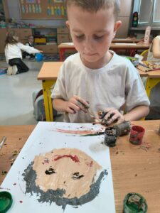 Dzieci siedzą przy stolikach i w skupieniu oddają się pracy twórczej.