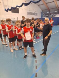 Przedstawia Mikołaja Durskiego, który trzyma dyplom za 4 miejsce zdobyte w turnieju. Za nim znajduje się cała reprezentacja SP Czerwonak. Obok jest organizator zawodów Pan Piotr Paupa. Widać jeszcze trzy reprezentacje, które zajęły odpowiednio miejsca od trzeciego do pierwszego.