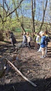 Uczniowie stojący w lesie aktywnie uczestniczą w lekcji outdoorowej.