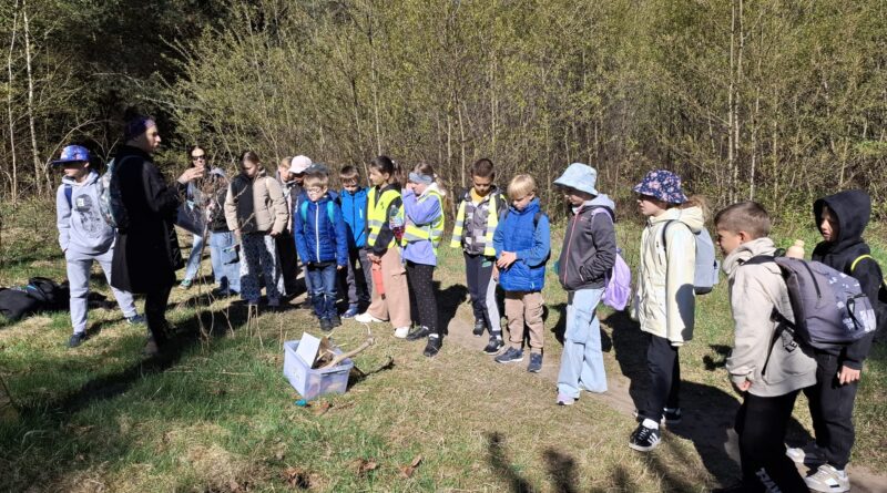 Uczniowie stojący w lesie aktywnie uczestniczą w lekcji outdoorowej.