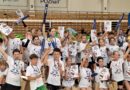 Na zdjęciu widać wszystkich zawodników i zawodniczki biorących udział w XVI edycji ENEA Mini CUP. Jest to zdjęcie zbiorowe. Wszyscy mają na sobie białe koszulki otrzymane od organizatora ENEA ENERGETYK Poznań. Ustawieni są pod siatką. W tle widać kolorowy, duży tor przeszkód „dmuchaniec” z którego korzystały dzieci podczas zawodów.