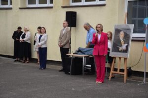 Pani Dyrektor Magdalena Zielenkiewicz przemawia do zgromadzonych uczniów, w tle widoczni są wicedyrektorzy Pani Iwona Hutek i Pan Adam Łukasiuk oraz inni przedstawiciele grona pedagogicznego.