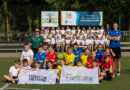 zdjęcie grupowe uczniów wraz z nauczucielami i gośiem, w tle uczniowie klas pierwszych. Przed dziećmi leżą flagi programu