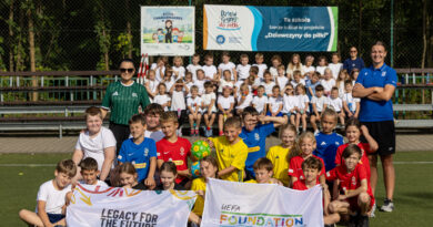 zdjęcie grupowe uczniów wraz z nauczucielami i gośiem, w tle uczniowie klas pierwszych. Przed dziećmi leżą flagi programu