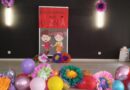 Szkolna scena udekorowana balonami i kolorowymi kwiatami oraz postaciami dziewczynki chłopca - czekająca na pierwszaki