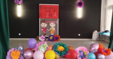Szkolna scena udekorowana balonami i kolorowymi kwiatami oraz postaciami dziewczynki chłopca - czekająca na pierwszaki