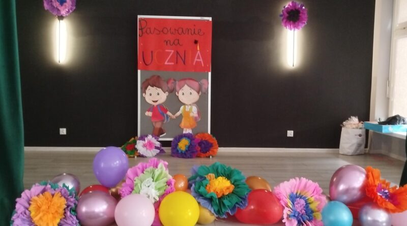 Szkolna scena udekorowana balonami i kolorowymi kwiatami oraz postaciami dziewczynki chłopca - czekająca na pierwszaki